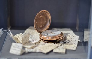 Eine goldene Taschenuhr liegt auf kleinen handschriftlichen Notizzetteln