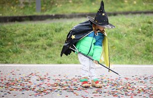 Ein verkleidetes Kind sammelt an Halloween Kronkorken mit einer Greifzange auf.