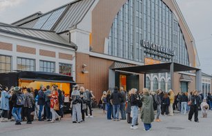 Die Halle für aktuelle Kunst ist eine ehemalige Markthalle. Vor ihr stehen ein Foodtruck und viele Menschen, die sich unterhalten. 